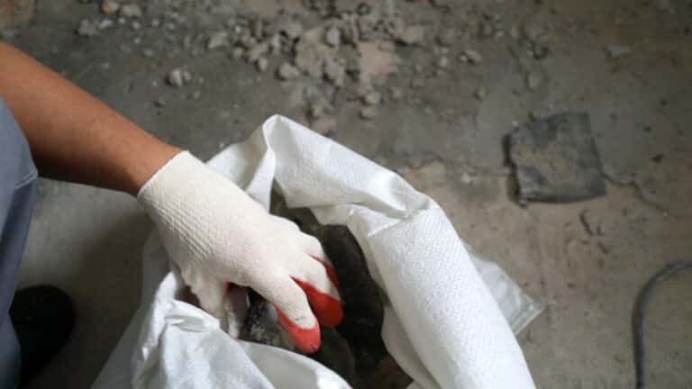 Builder cleaning room from old concrete and bricks after demolition jobs. A worker removes garbage with a dustpan. Worker sweeps construction debris with a broom.