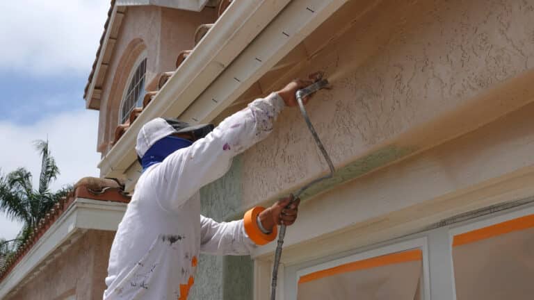 Professional contractor using a spray paint gun to paint the stucco on a home